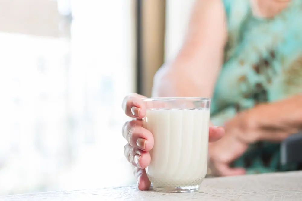 person holding a white protein drink in a clear glass